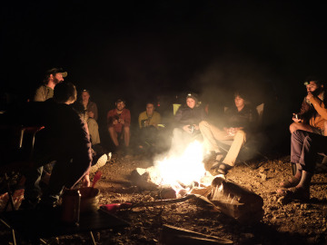Students sit around the camp fire talking and laughing. Image by Harry Tang.