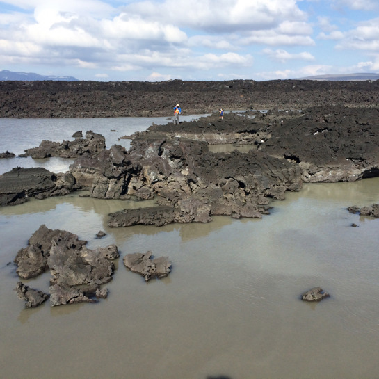 The river adjacent to the lava flow fluctuates daily with the amount of glacial meltwater generated upstream, indicated by the high-water marks along the edges of the flow. Scientists explore the hydrologic connections between the level of the river and the hot springs emerging downstream.