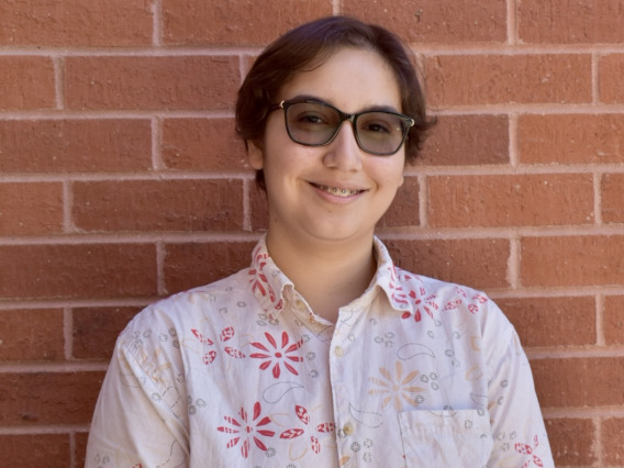 Person with short brown hair smiling at camera, standing in front of a red brick wall