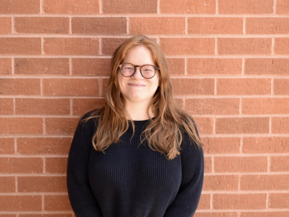 person smiling at camera against brick wall