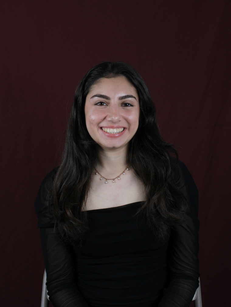 Student smiling at camera with long dark hair against a dark background