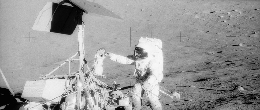 Charles Conrad examines Surveyor's TV camera prior to detaching it on Nov. 20, 1969. The Apollo 12 lunar module is in the background. (Image: NASA)