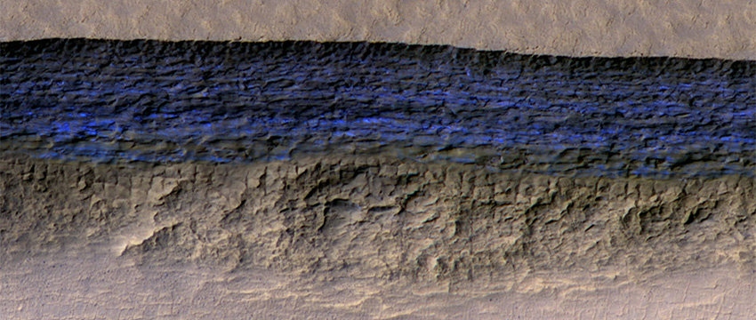At this pit on Mars, the steep slope at the northern edge (toward the top of the image) exposes a cross section of a thick sheet of underground water ice. The image is from the HiRISE camera on NASA's Mars Reconnaissance Orbiter, with an enhanced-color central swath between grayscale on each side. (Image: NASA/JPL-Caltech/UA/USGS)