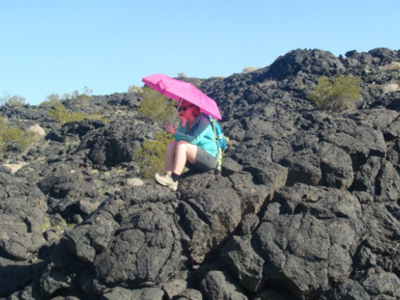 A University of Arizona Lunar and Planetary Laboratory student holds a bright umbrella over the spot where she found geologic contact between two different lava flows during a trip to Amboy Crater in California's Mojave Desert. (Photo: Ali Bramson)