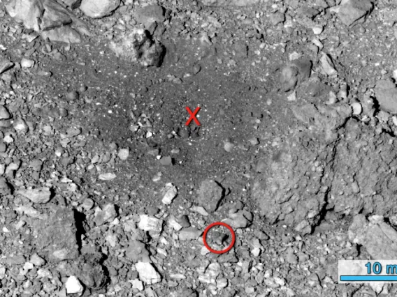 The Nightingale sample site after the TAG event. The red "X" indicates the approximate location where OSIRIS-REx contacted the asteroid's surface. The red circle shows the same boulder that was circled in the before image. NASA/Goddard/University of Arizona