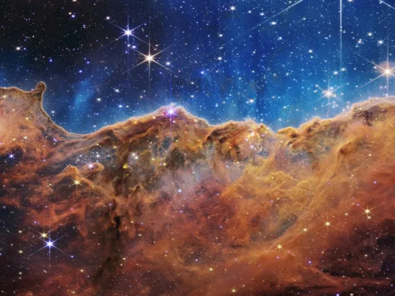 This landscape of what looks like mountains and valleys speckled with glittering stars is actually the edge of a nearby, young, star-forming region called NGC 3324 in the Carina Nebula. Captured in infrared light by NASA's Webb Telescope, this image reveals for the first time previously invisible areas of star birth. NASA, ESA, CSA, and STScI