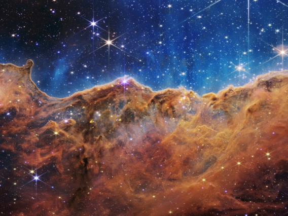 This landscape of what looks like mountains and valleys speckled with glittering stars is actually the edge of a nearby, young, star-forming region called NGC 3324 in the Carina Nebula. Captured in infrared light by NASA's Webb Telescope, this image reveals for the first time previously invisible areas of star birth. NASA, ESA, CSA, and STScI