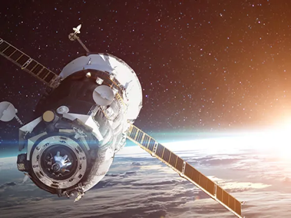 Satellite flying through space over Earth with sun setting in the distance.