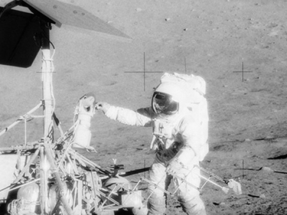 Charles Conrad examines Surveyor's TV camera prior to detaching it on Nov. 20, 1969. The Apollo 12 lunar module is in the background. (Image: NASA)