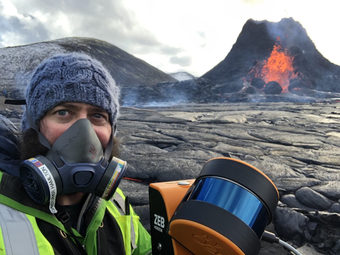 Christopher Hamilton stands in front of an erupting Icelandic volcano.