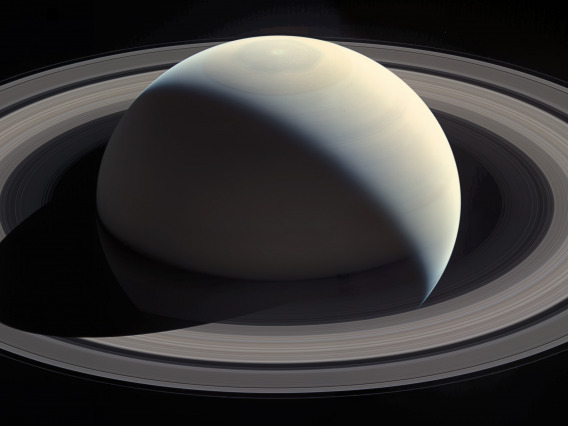 NASA image of Saturn with sunlight from behind the planet and to the right illuminating the planet disk and rings and throwing a black shadow onto a portion of the bottom left-hand portion of the rings.