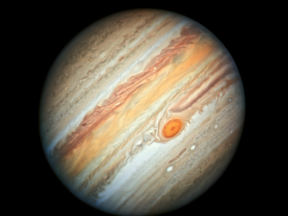 NASA image of Jupiter with dark and light grey-brown swirling stripes of clouds nearer to the poles and more vibrant red, orange and white cloud bands nearer to the equator. The Great Red Spot is near the center above a series of small, bright white circular storm features.